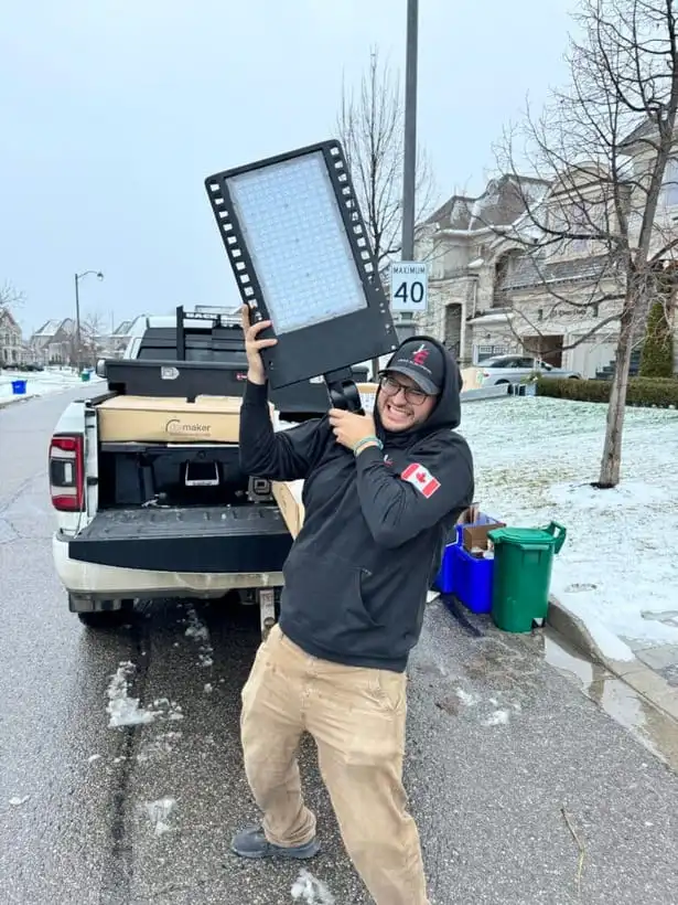 A Jayco Electrical crew member in a branded hoodie carrying a large commercial LED fixture on a snowy Greater Toronto Area street